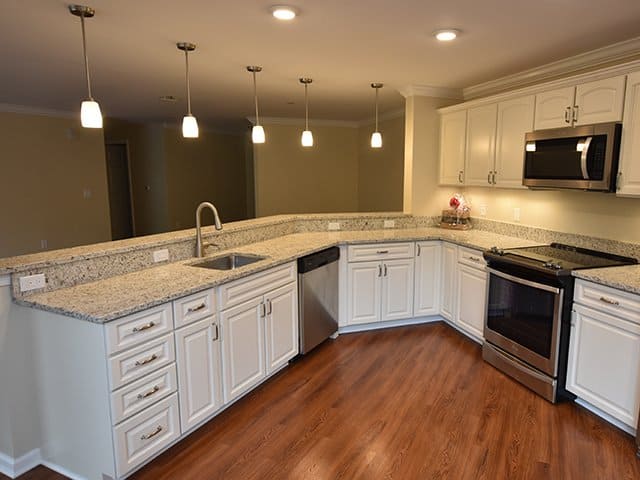an off-white kitchen with angled peninsula and granite countertops inside of a Linden Ponds apartment in Hingham, MA