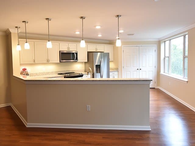 an off-white kitchen with angled peninsula and granite countertops inside of a Linden Ponds apartment in Hingham, MA