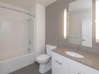 a modern white single bath vanity with quartz vanity top, a white toilet and tub/shower in an Ames Shovel Works apartment in North Easton, MA