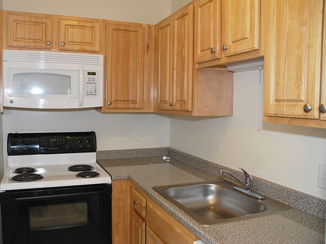 raised panel kitchen cabinets and a laminate countertop with a white, over the stove microwave and black and white electric stove in a Northgate apartment home in Revere, MA
